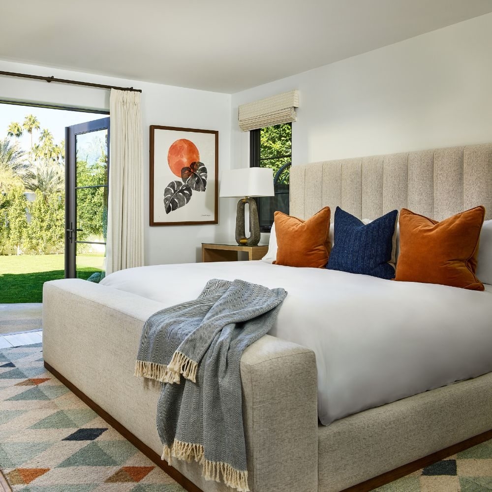 An upholstered bed with ivory bedding, blue and rust pillows, and a folded gray throw