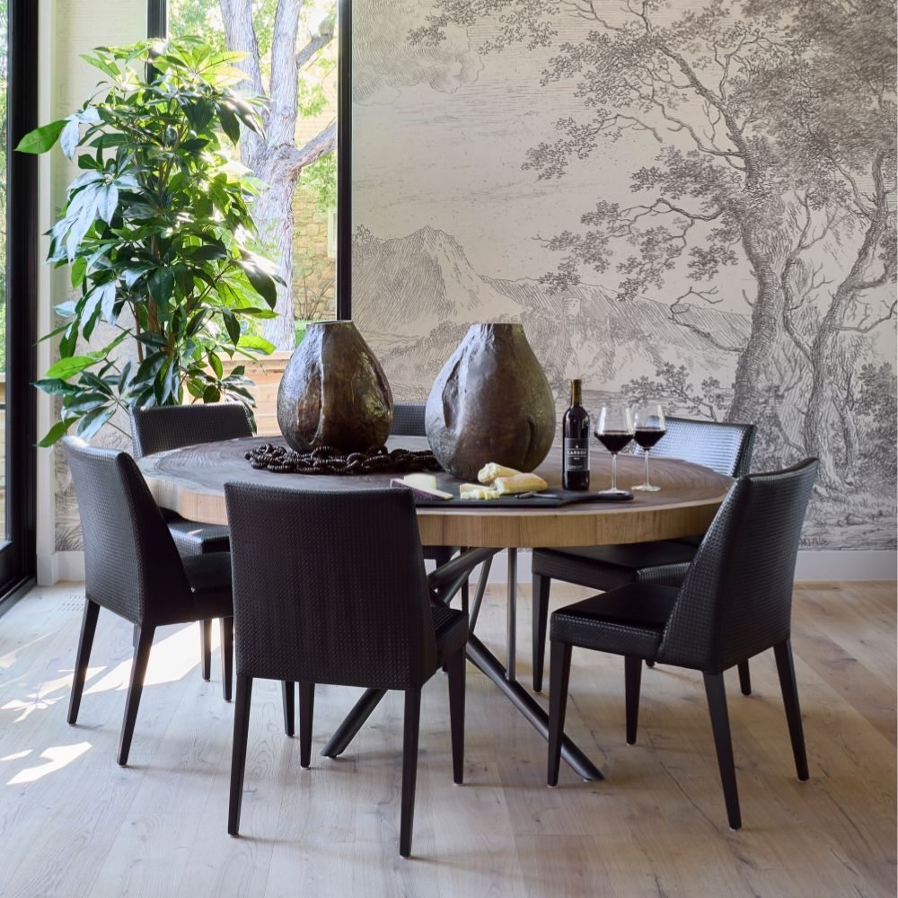 A round dining table with dark upholstered chairs, sculptural vessels, and a botanical wall mural