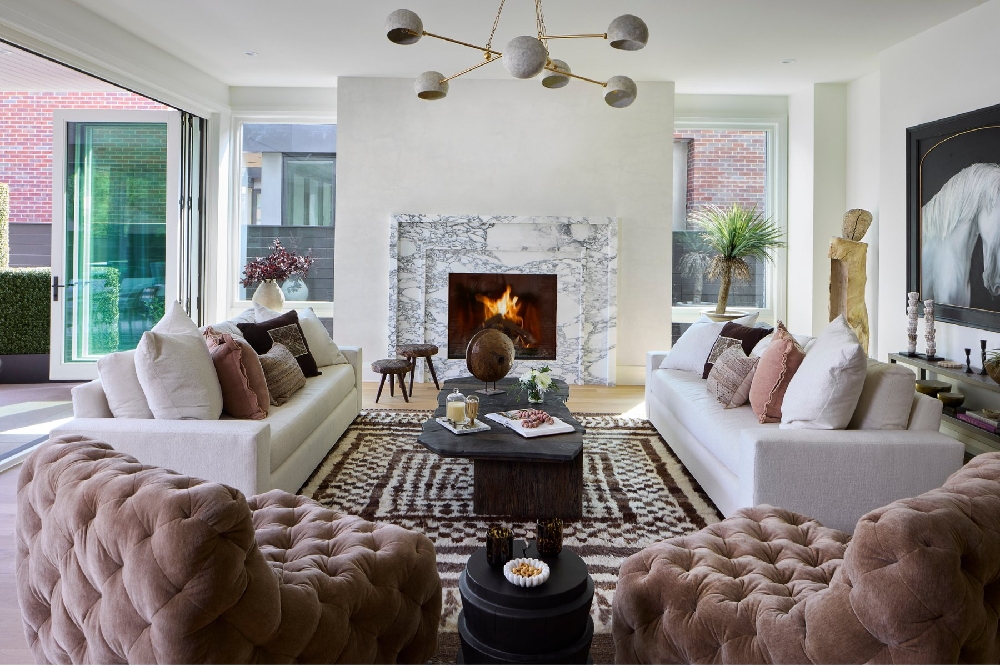 Two ivory sofas and rounded taupe chairs arranged around a dark coffee table and marble fireplace
