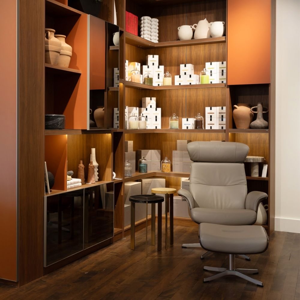 A gray lounge chair beside warm wood display shelves filled with decorative objects
