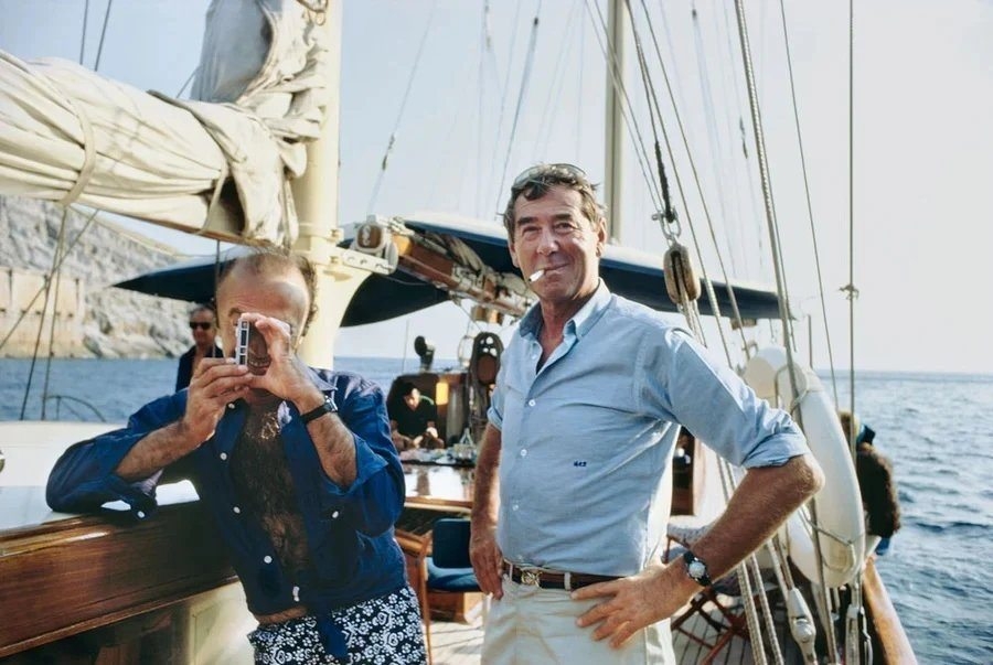 Slim Aarons standing aboard a boat in Italy in 1968 with a camera nearby