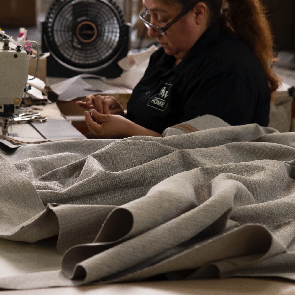 A craftsperson works at a sewing machine with pale upholstery fabric